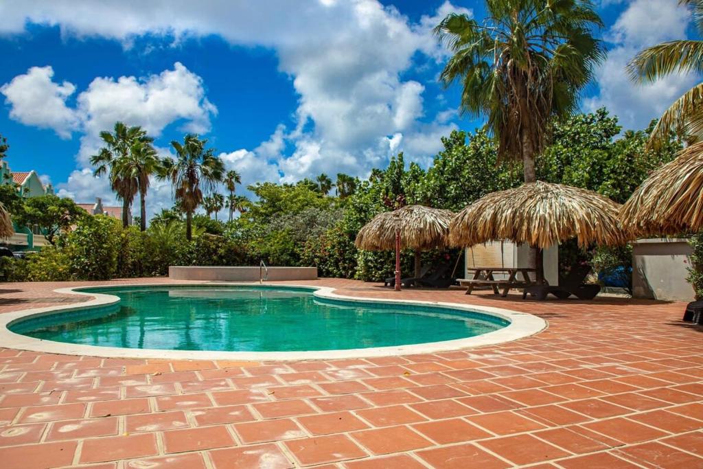 a swimming pool with a brick patio and palm trees at Caribbean Court Apartment Good Vibes in Kralendijk
