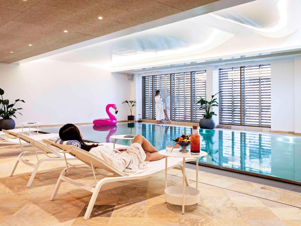 a woman laying on chairs next to a swimming pool at Pullman Paris Centre - Bercy in Paris