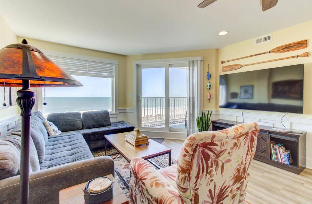 a living room with a couch and a table and a television at Carolina Surf - 3BR Condo with Stunning Ocean Views in Carolina Beach
