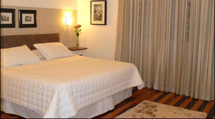 um quarto com uma grande cama branca e cortinas em Hotel Jardim Bulevard em Ituporanga