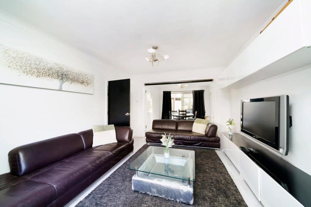 a living room with a leather couch and a tv at Chic 4BR Home with Ensuite bath and Cozy Garden in Dagenham