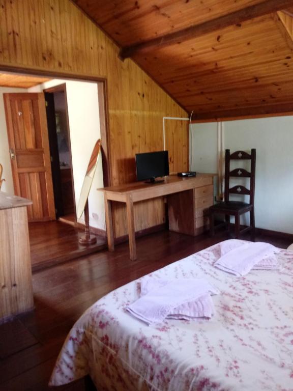 a bedroom with a bed and a desk with a television at Chalé Maringá in Bocaina de Minas