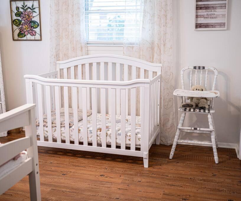 a white crib and a chair in a room at Family friendly getaway in North Richland Hills