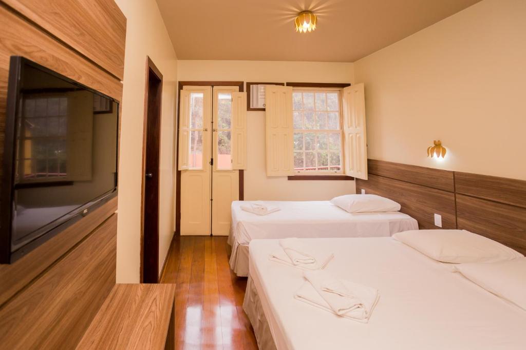 a room with two beds and a flat screen tv at Mirante Hotel in Ouro Preto