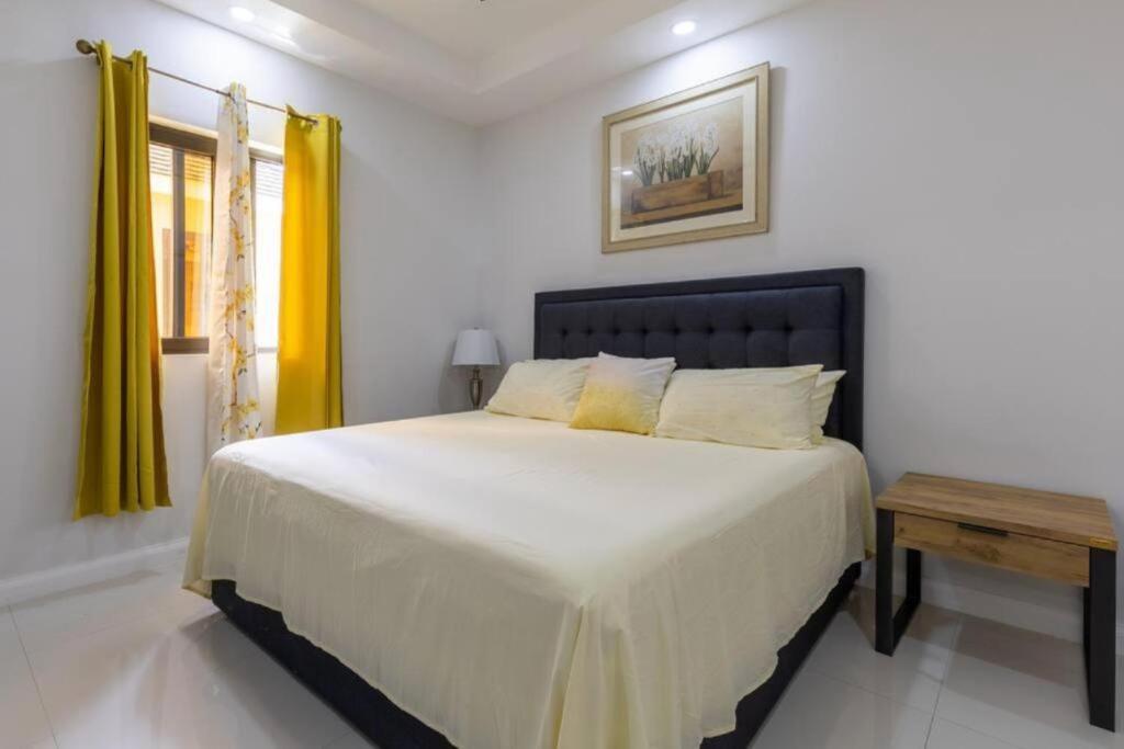 a bedroom with a large white bed with yellow curtains at Luxury Palm in Old Harbour