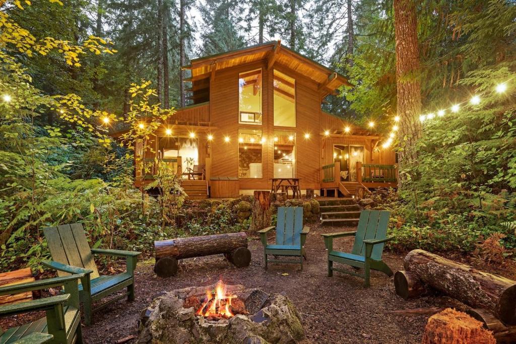 uma cabana de madeira na floresta com cadeiras e uma lareira em ZigZag Basecamp · Cozy Cabin Perfect for Nature Escapes w/ Hot Tub em Rhododendron