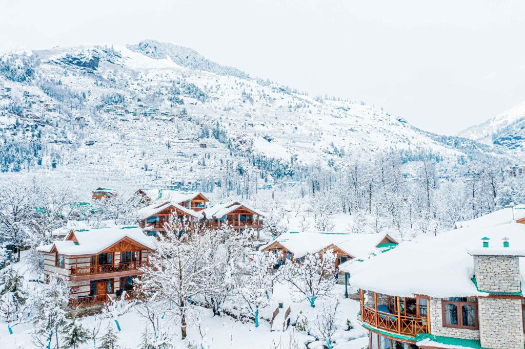 a resort covered in snow with mountains in the background at Storii By ITC Hotels Urvashis Retreat, Manali in Manāli