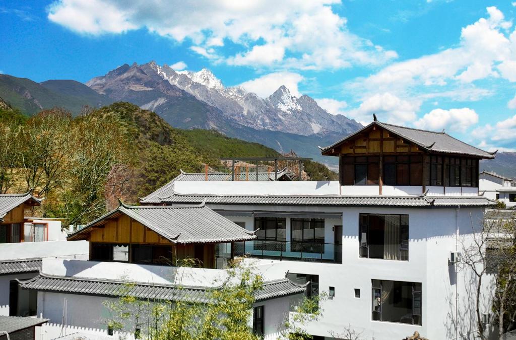a white building with mountains in the background at Lijiang Hengchang Baoyin Mohuakai Inn in Lijiang