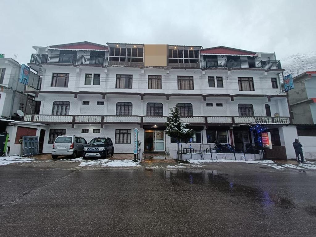 a large white building with cars parked in front of it at Hotel Badrinath in Badrinath