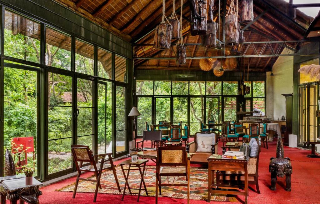 Habitación grande con sillas, mesas y ventanas. en Jim's Jungle Retreat, en Rāmnagar