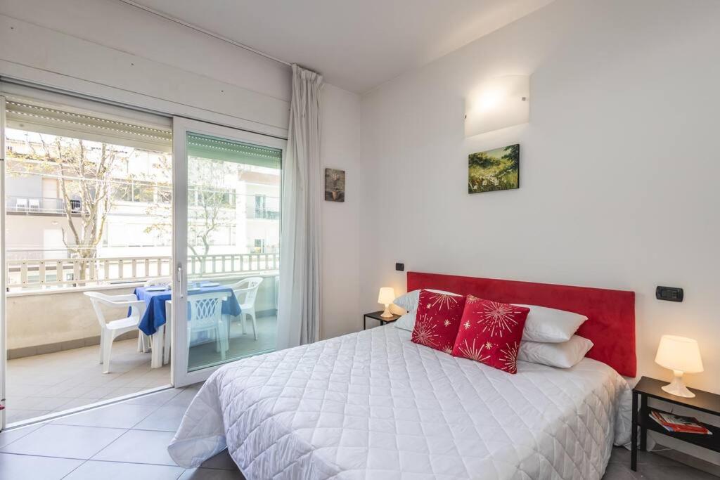 Cette chambre comprend un lit avec des oreillers rouges et un balcon. dans l'établissement Exclusive: Fronte Mare con Terrazzo e Parcheggio, à Rimini