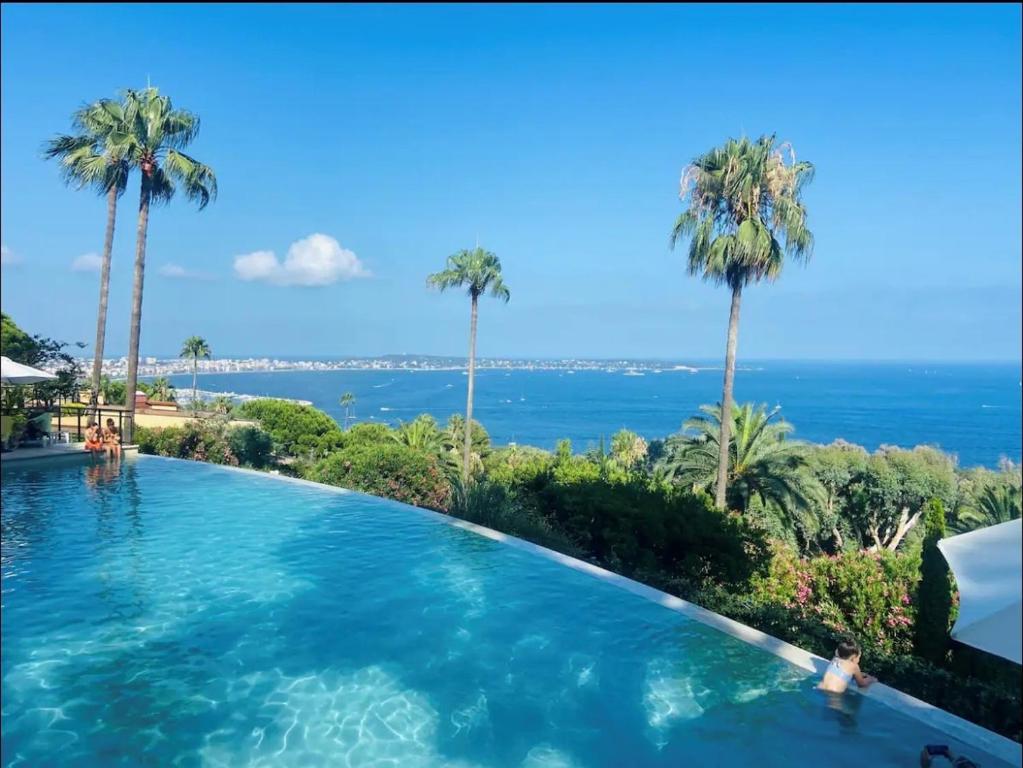 une piscine avec des palmiers et l'océan en arrière-plan dans l'établissement Appart 2P Vue Mer Panoramique Cannes Eden, à Vallauris
