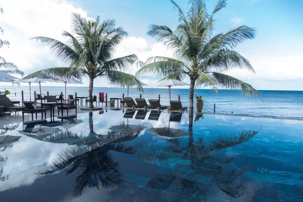 a swimming pool with palm trees and the ocean at Palmy Luxury Beach Phú Quốc in Phu Quoc