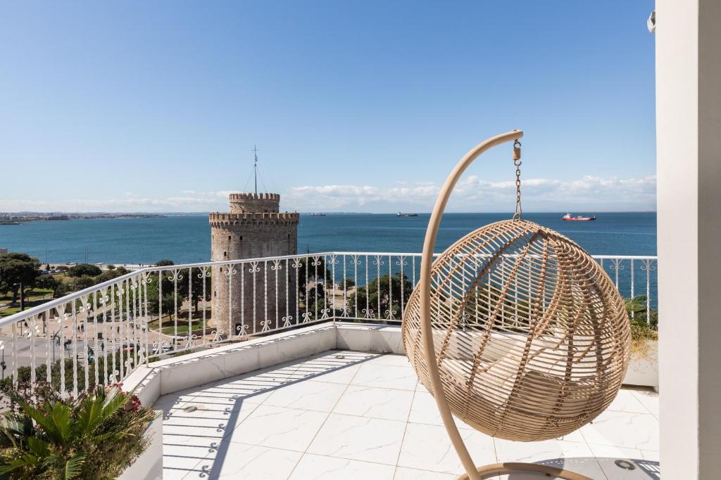 a rattan chair on a balcony with a view of the ocean at Aria, Lux seafront apt with White Tower view in Thessaloniki