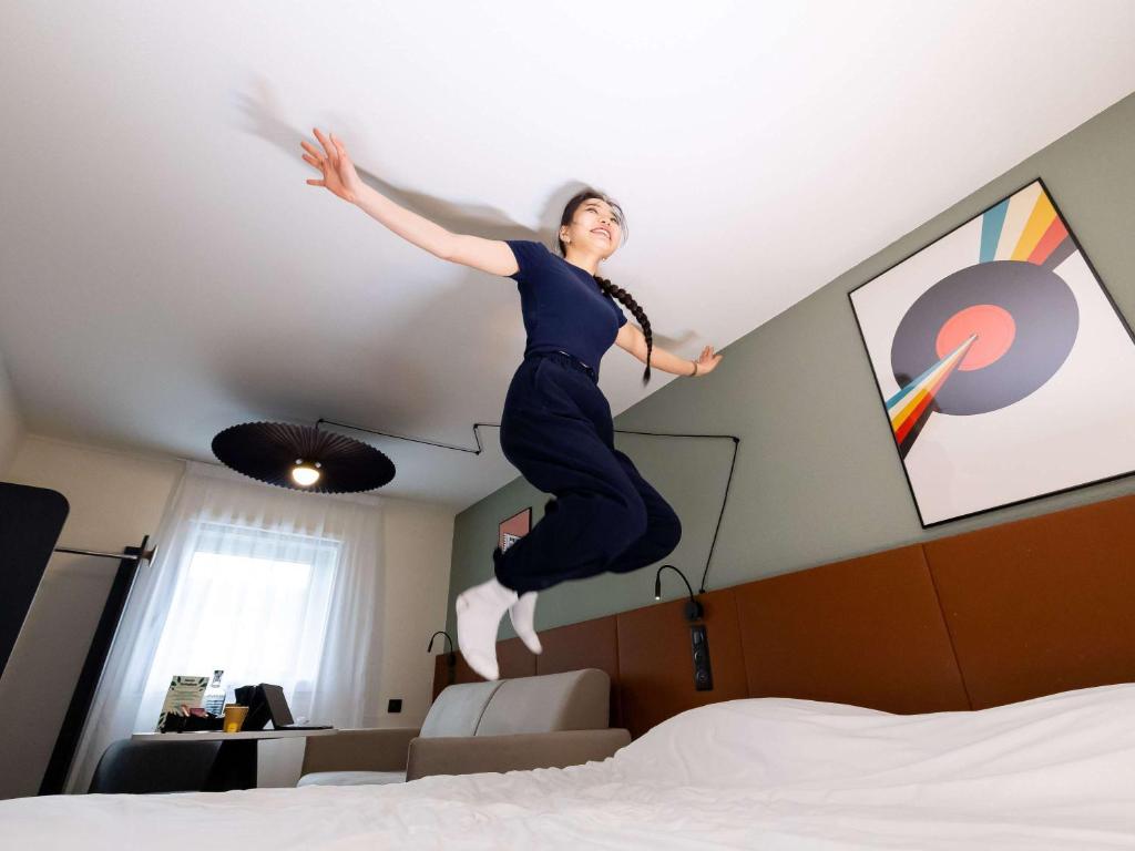 a woman jumping in the air on a bed at ibis Bordeaux Centre Meriadeck in Bordeaux