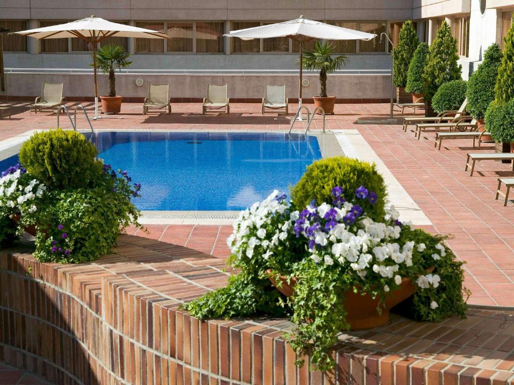 una piscina con macetas de flores, mesas y sillas en Novotel Campo De Las Naciones, en Madrid
