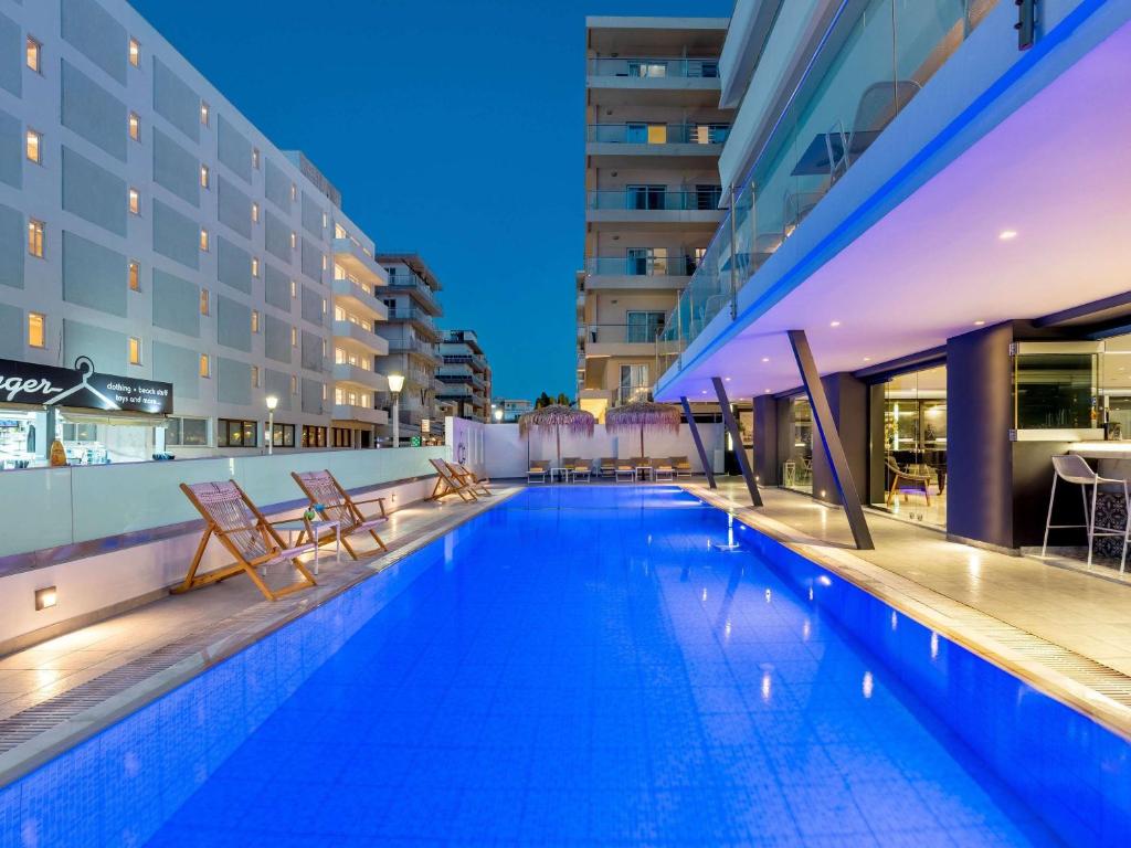 una piscina con due sedie e un edificio di Mercure Rhodes Alexia Hotel & Spa a Città di Rodi