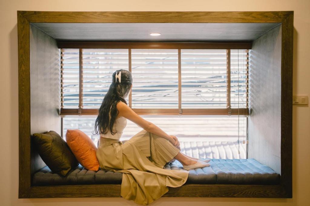 チェンカーンにあるThe Folkster House Chiangkhanの窓枠に腰掛けて窓の外を見下ろす女