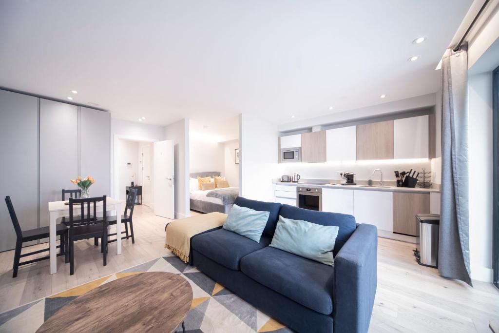 a living room with a blue couch and a kitchen at Spacious & Smart Studio Flat with Balcony - Zone1 in London