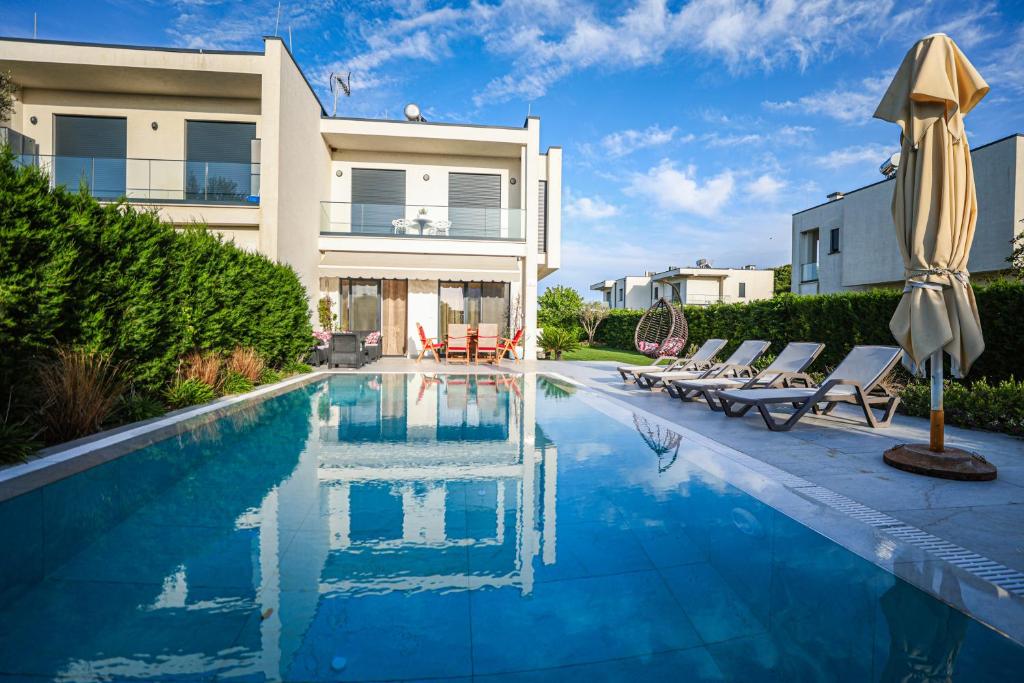 a swimming pool with chairs and an umbrella next to a house at Vila 29 Valamar in Durrës