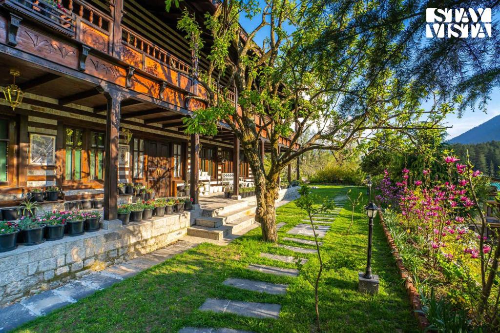 a building with a tree and flowers in the yard at StayVista at Snowdrop House - 5BR, 4BR, 3BR, 2BR with Snowcapped Mountain View on Main Highway Manali in Manāli