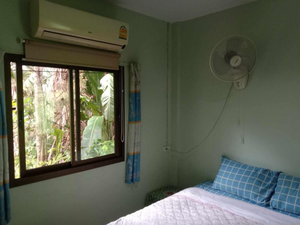 a bedroom with a bed and a window with a fan at kamrai resort apartment in Ban Bang Bao