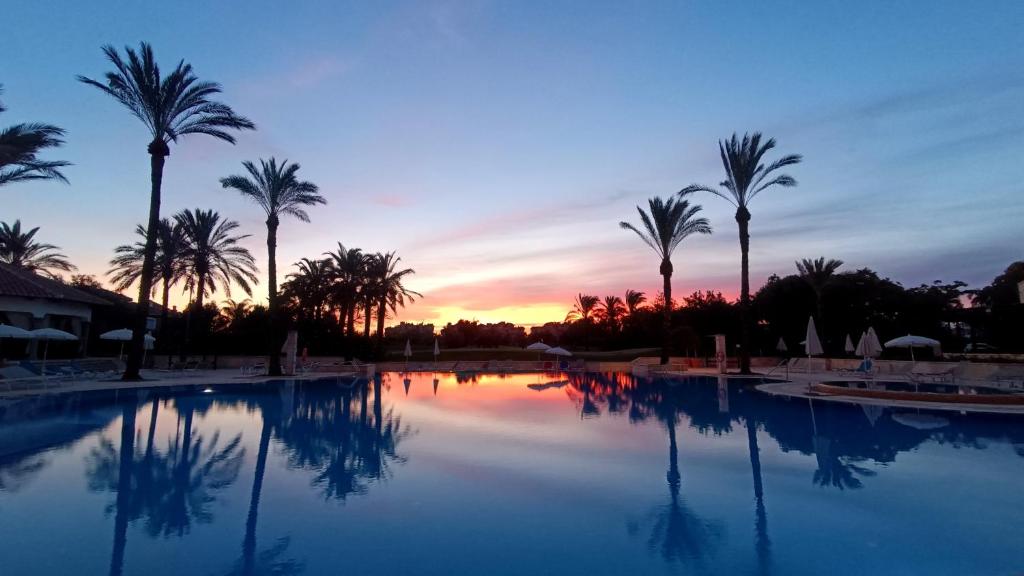 une grande piscine avec des palmiers et un coucher de soleil dans l'établissement Casa Amarillo Mar Menor Golf Resort, à Murcie
