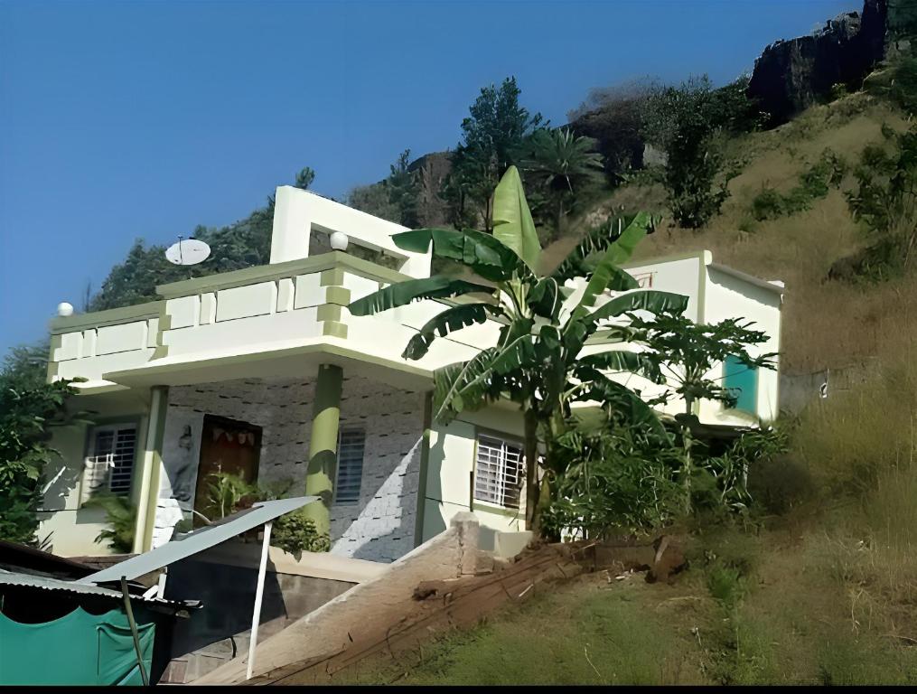 a white house with a palm tree in front of a hill at Vrundavan in Panchgani