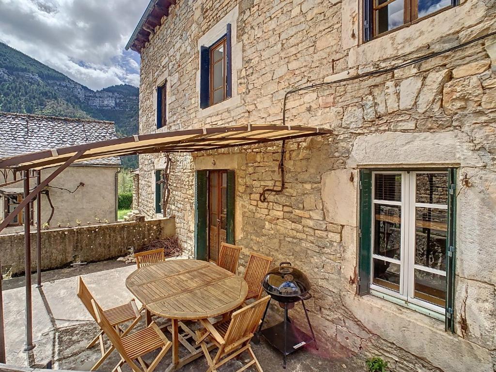 un patio avec une table, des chaises et un parasol dans l'établissement Gorges du Tarn gîte en pierres avec terrasse, à Quézac