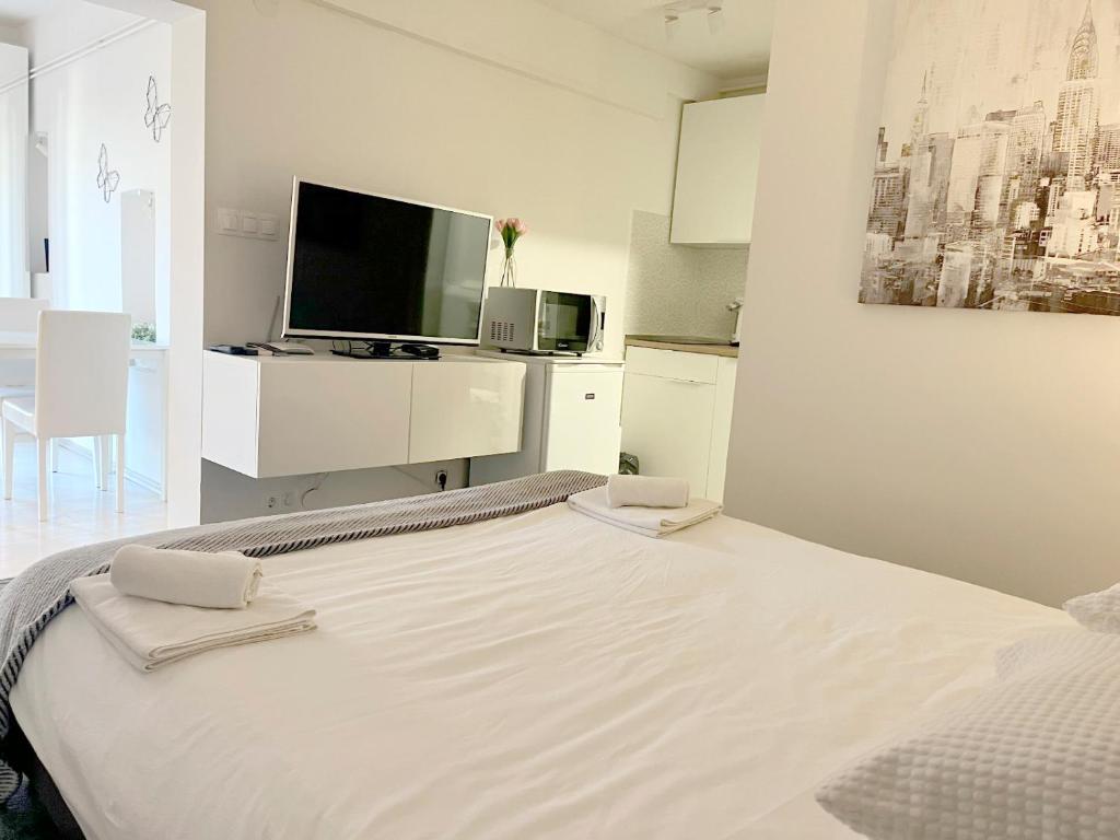 a white bedroom with a large bed and a tv at Bed & Bike Zagreb studio apartment in Zagreb