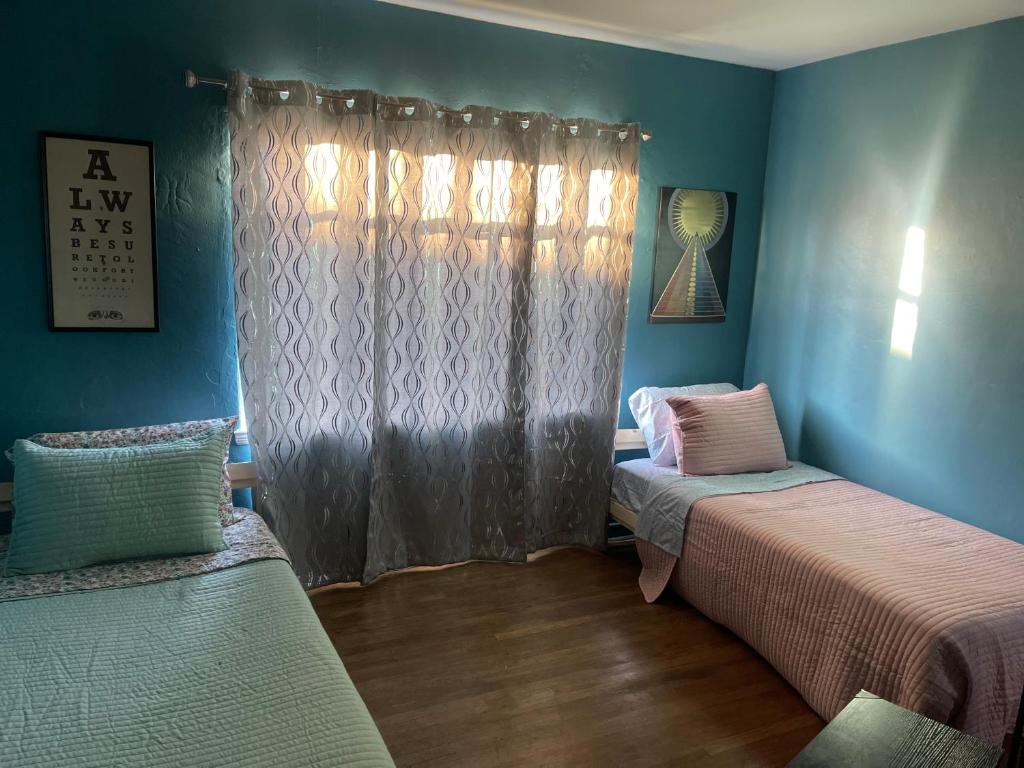 オークランドにあるH.U.S.H (Happy Your Staying Here!) Short Term Rentalの青い壁の客室で、ベッド2台、窓が備わります。