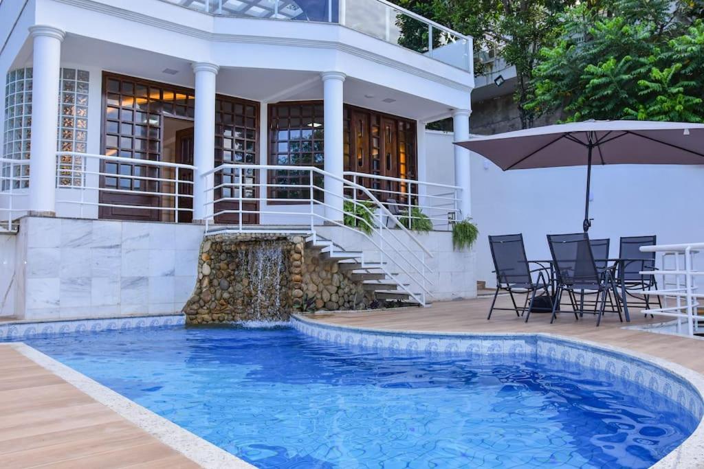 a house with a swimming pool with chairs and an umbrella at Casa Oásis do Moreno 6 in Vila Velha