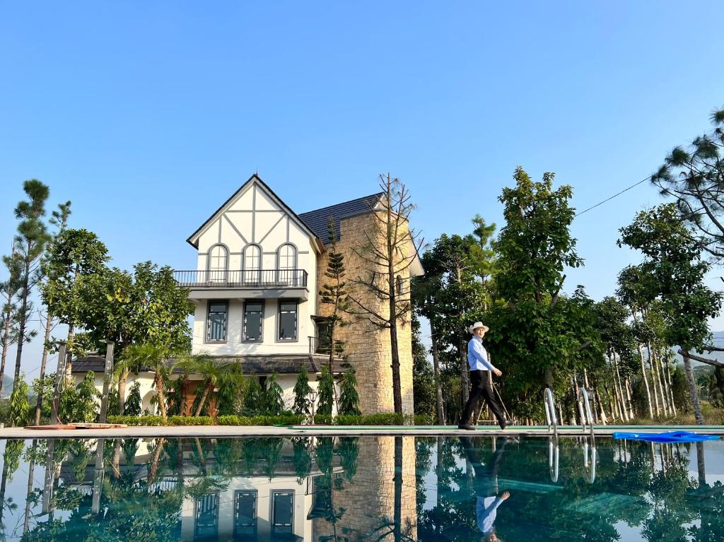 Ein Mann geht vor einem Haus neben einem Swimmingpool entlang. in der Unterkunft Valentina Castle - Melorita Hòa Lạc in Hanoi