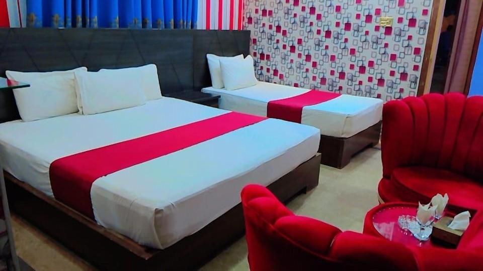 um quarto com 2 camas e 2 cadeiras vermelhas em Shelton One Hotel em Multan