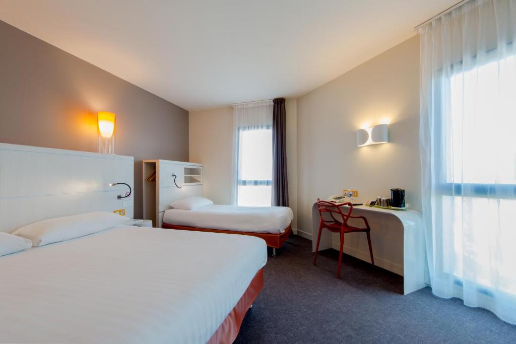 a hotel room with two beds and a desk at Hôtel Confort La Rochelle Centre les Minimes in La Rochelle