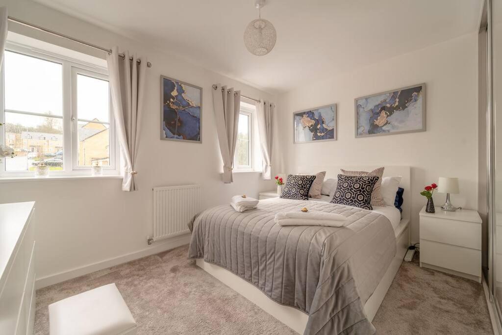 a white bedroom with a bed and two windows at Stylish 3 Bed, 3 Bath, Garden & Drive for 2 cars in Colne