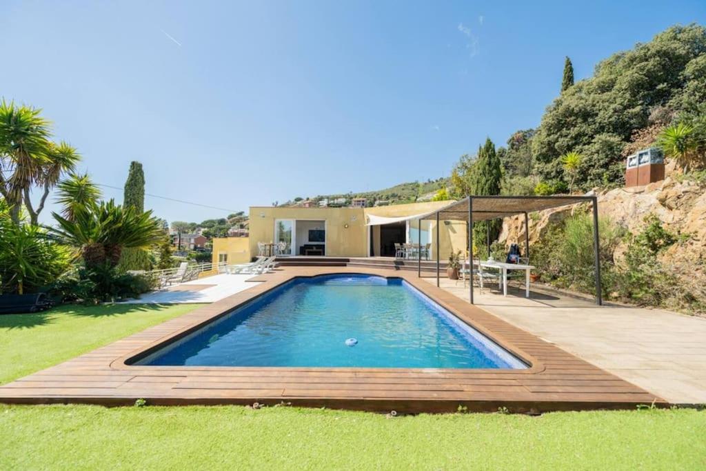 a swimming pool with a wooden deck and a house at Casa Mediterrani & piscina comunitaria junto Barcelona in Alella
