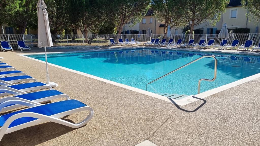 - une piscine avec des chaises bleues et un parasol dans l'établissement Le Hameau du Moulin, à Montignac