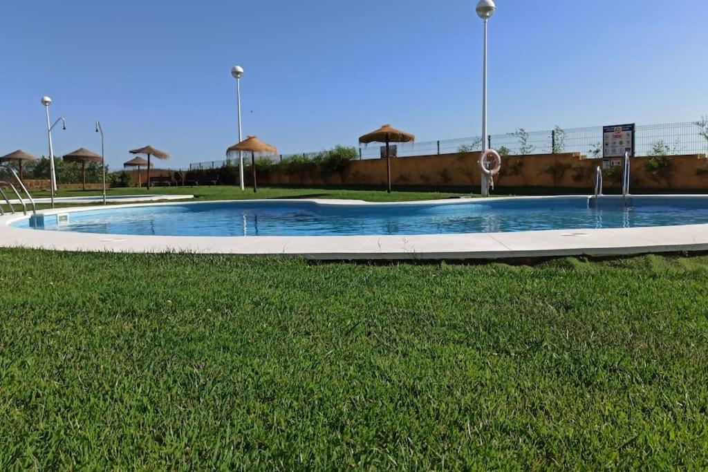 a swimming pool with an umbrella in the grass at La Colina Playa&Golf in Huelva