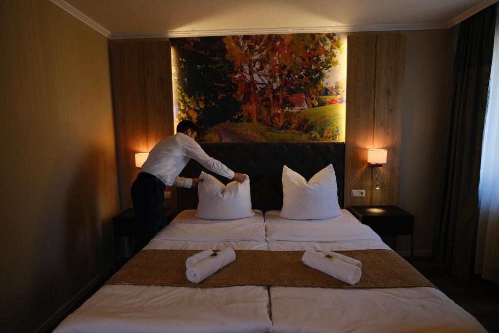 a man putting pillows on a bed in a hotel room at PARKHOTEL - Rosarium in Uetersen