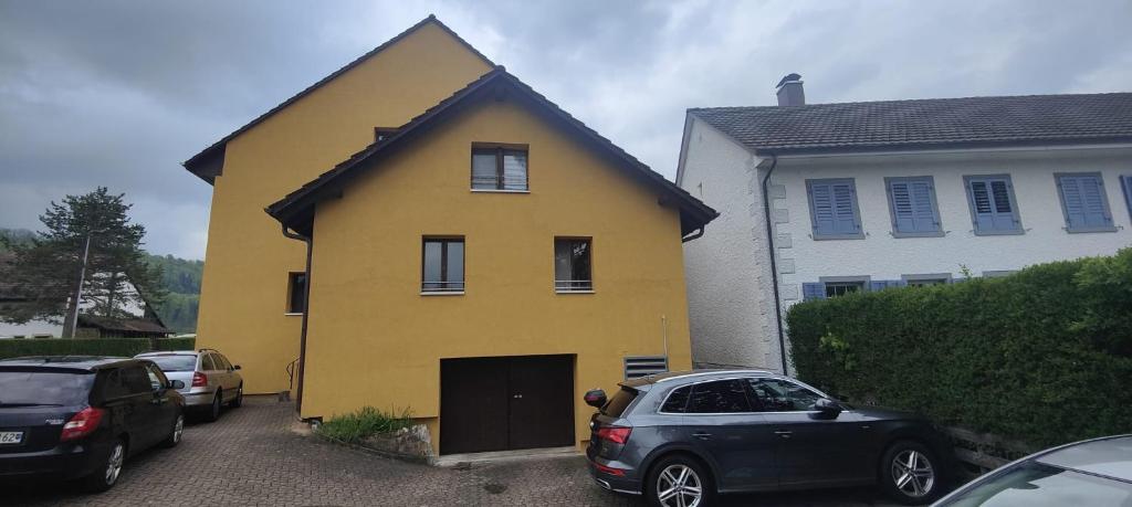 een geel huis met auto's geparkeerd op een parkeerplaats bij Gästehaus Spring Herznach in Herznach