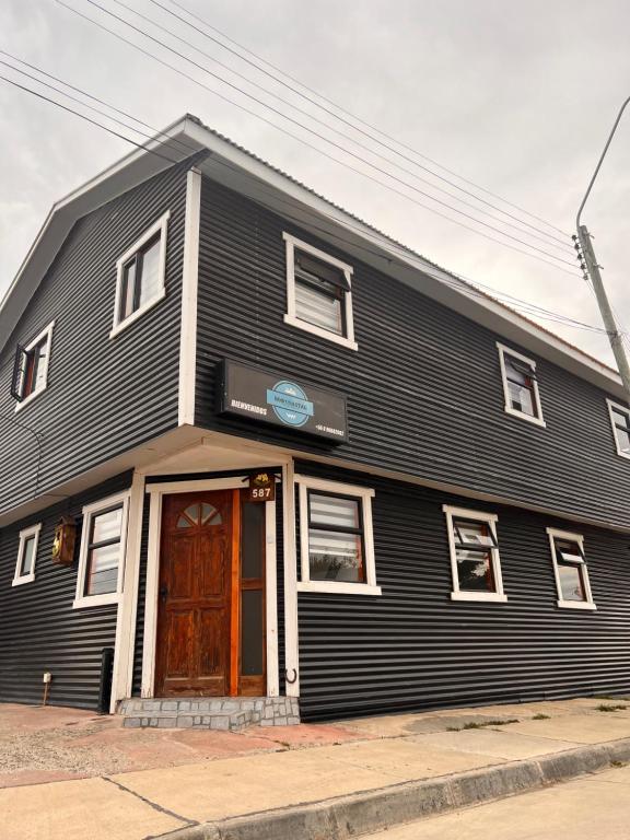 um edifício preto com uma porta castanha numa rua em Hostal B&B Coastal Natales em Puerto Natales