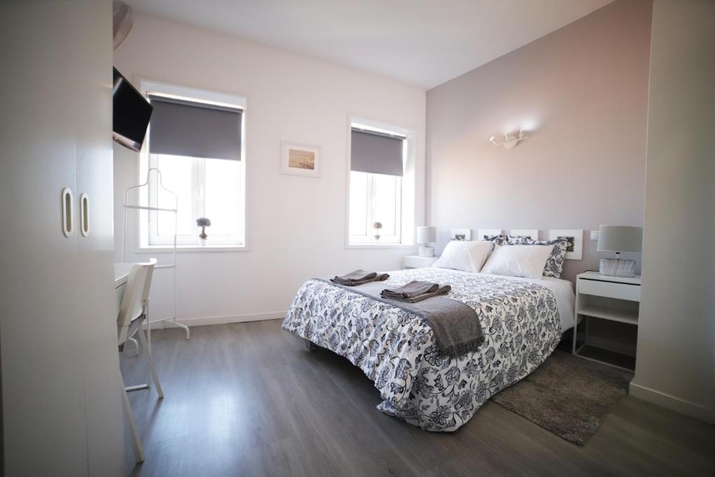 a bedroom with a bed and a desk and two windows at Guest House Triunfo in Porto