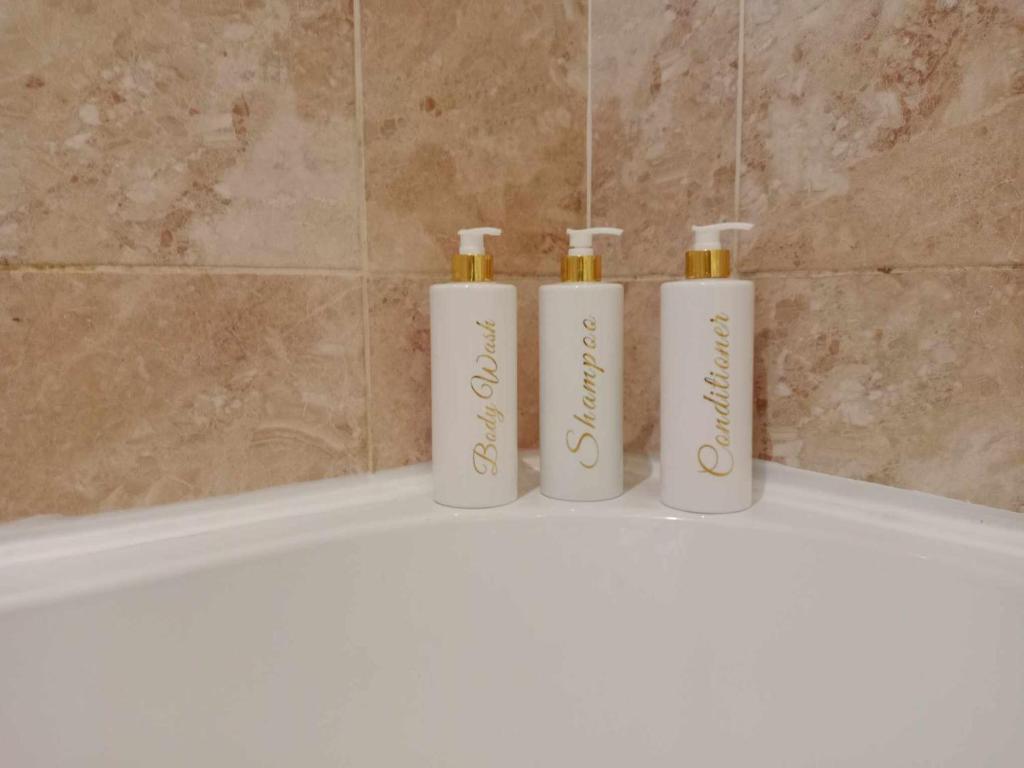 three white bottles sitting on the edge of a bath tub at Monmouth Aylesbury Retreat in Buckinghamshire