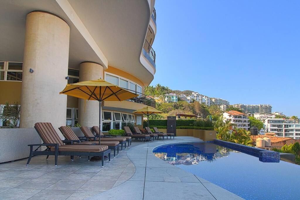 a hotel with chairs and umbrellas next to a swimming pool at Pinnacle Resort-Style Condo - Luxurious Balcony in Puerto Vallarta
