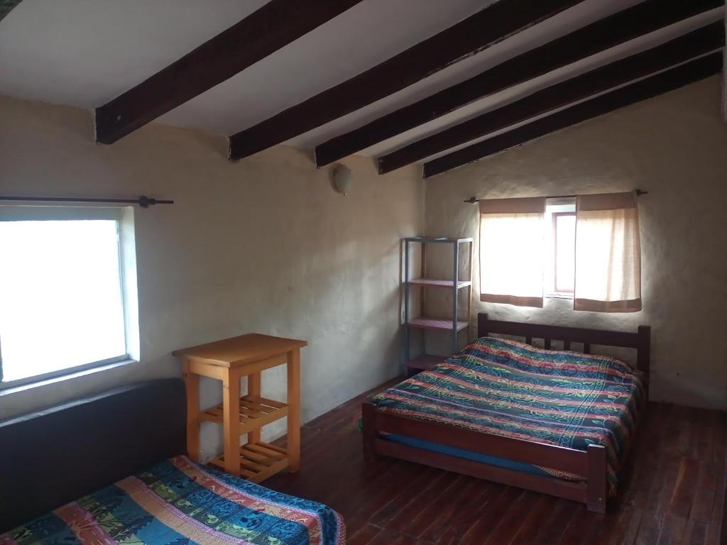 1 dormitorio con 2 camas, mesa y 2 ventanas en Casa Loto, en Samaipata