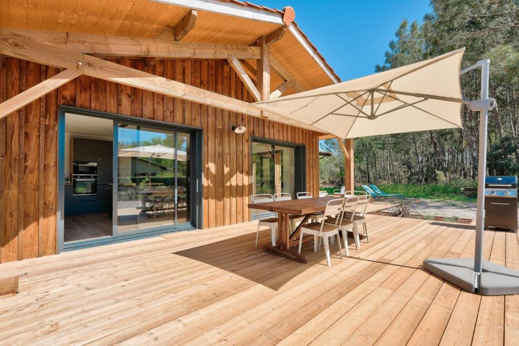 a wooden deck with a table and an umbrella at Peaceful house on the edge of a forest in Sanguinet