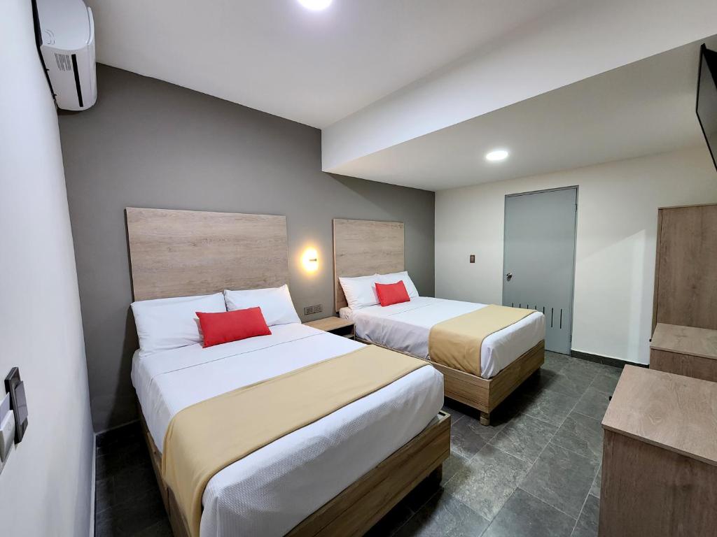 Hotel Roque في توريون: سريرين في غرفة الفندق مع وسائد حمراء