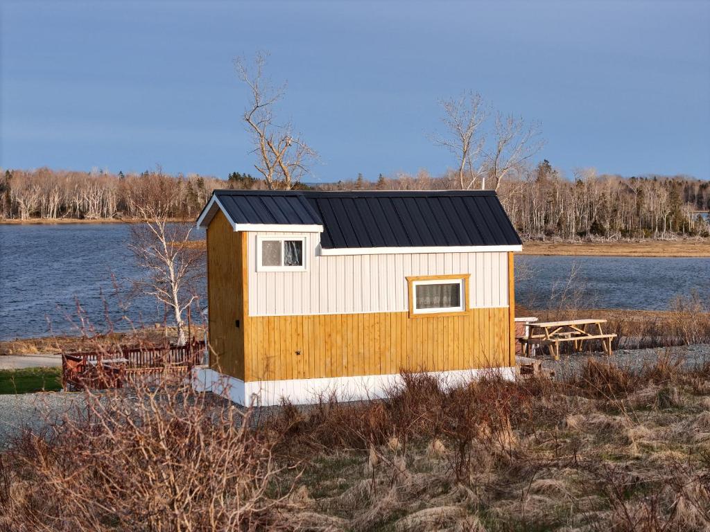 a small yellow and white building next to a body of water at Waterfront Tiny House near Pomquet Beach in Antigonish