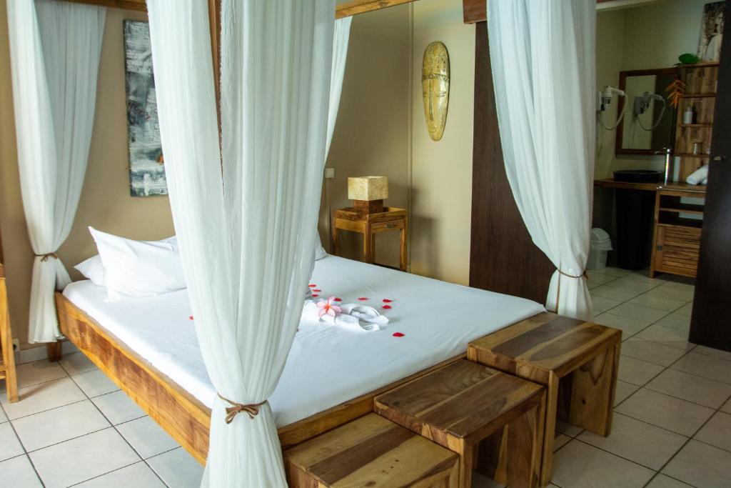 a bedroom with a bed with white curtains and red peppers at Hotel Ylang Ylang in Saint-Gilles-les-Bains